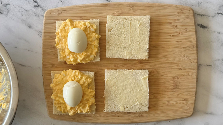 Open faced egg salad sandwiches with whole eggs on top of egg salad