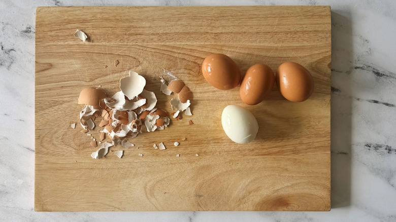 Eggs and one peeled egg on wooden board