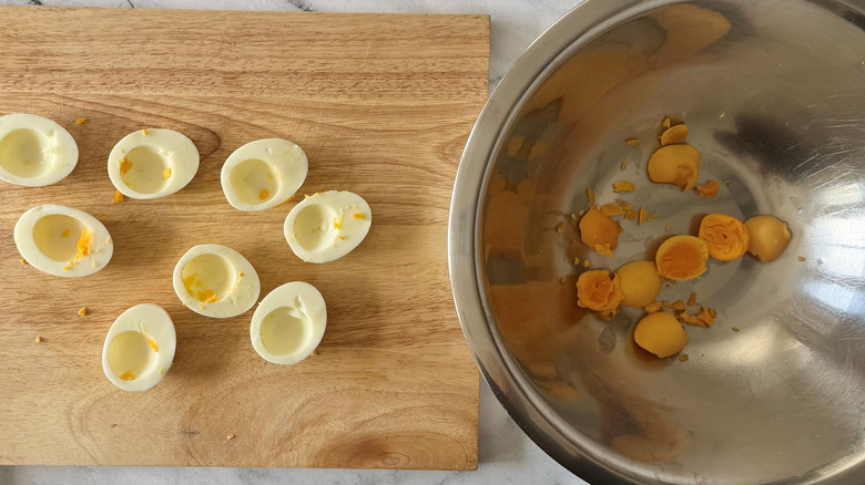 Hard boiled egg whites on wooden board next to yolks in bowl