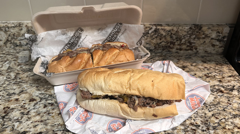 Takeout box of Firehouse Subs steak and cheese melt next to Jersey Mike's philly cheesesteak on wrapper on countertop