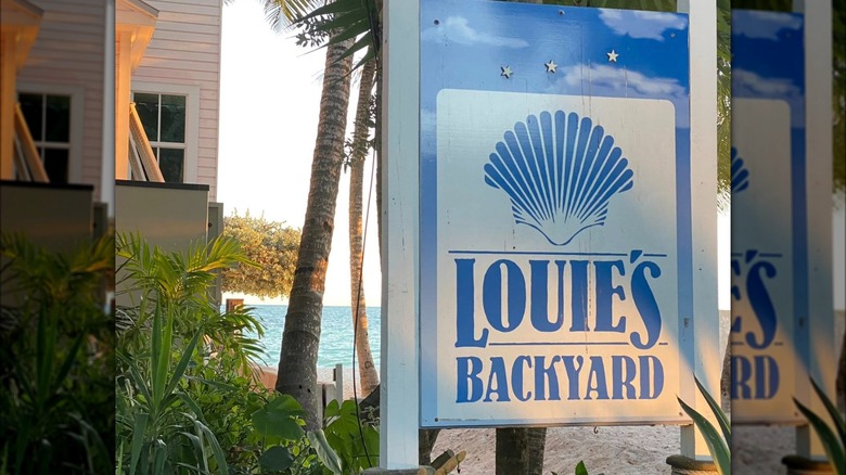 A shot of Louie's Backyard outdoor signage among palm trees and the beach