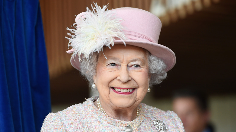 Queen Elizabeth, smiling, in a pink hat with feathers