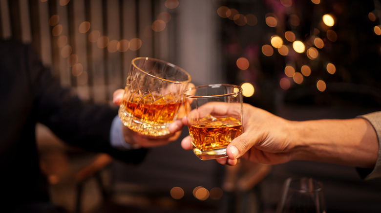 Two people toasting with glasses of whiskey in tumbler glasses.