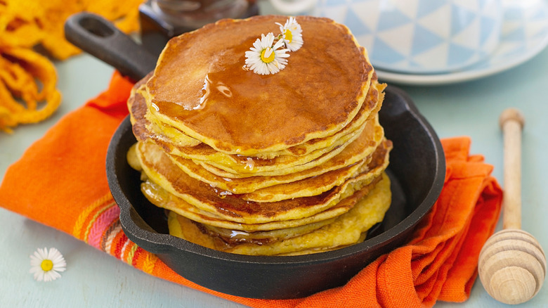 Johnny cakes stacked on one another in a cast iron skillet topped with dandelions