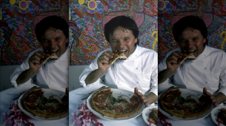 Wolfgang Puck biting into a slice of his frozen pizza against a graffiti wall