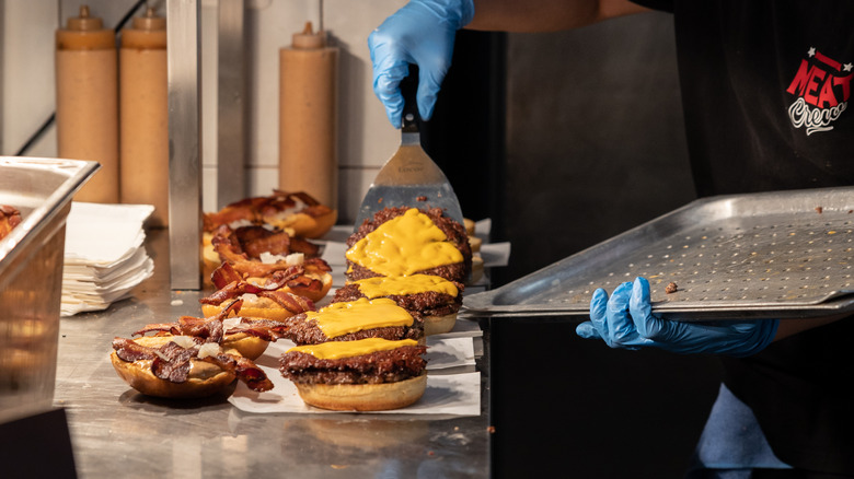 Chef assembling row of cheeseburgers with bacon