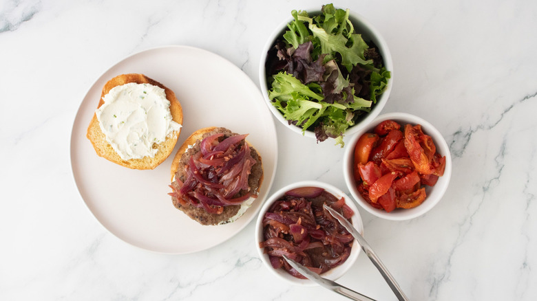 Lamb burger topped with red wine onions next to bowls of toppings