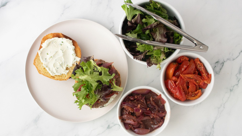 Lamb burger topped with greens next to bowls of toppings