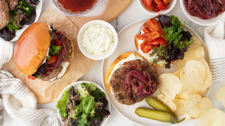 Lamb burgers on plates with toppings and potato chips
