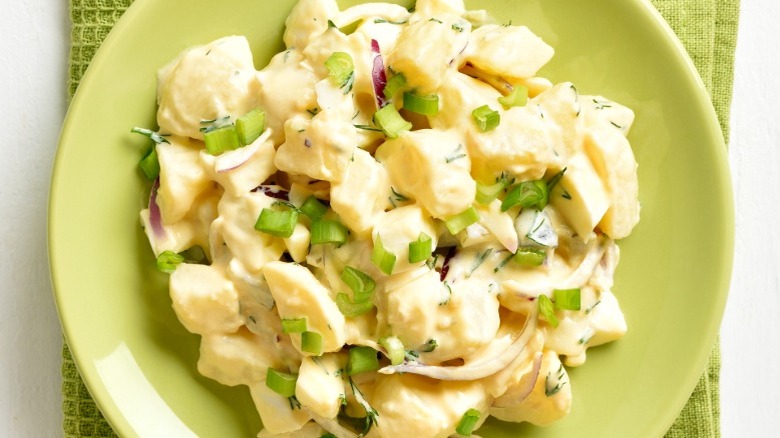 Green bowl of potato salad with scallions, red onion, and egg