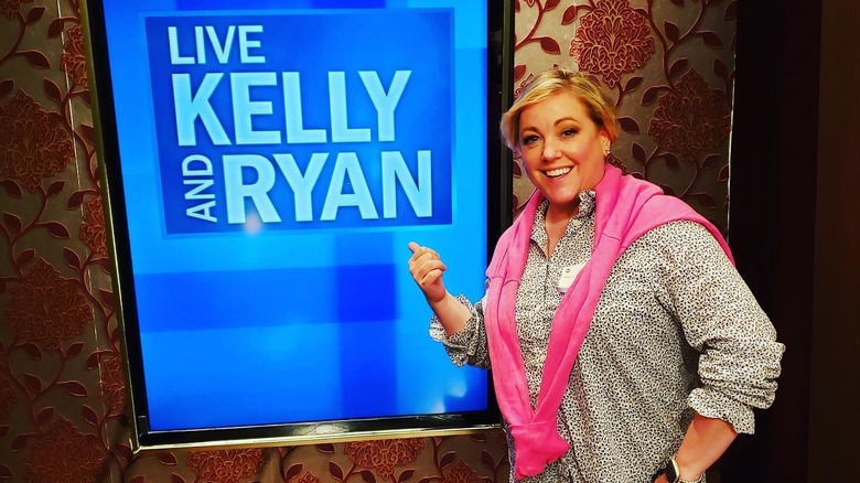 Julia Collin Davison smiles and points at Live With Kelly and Ryan sign