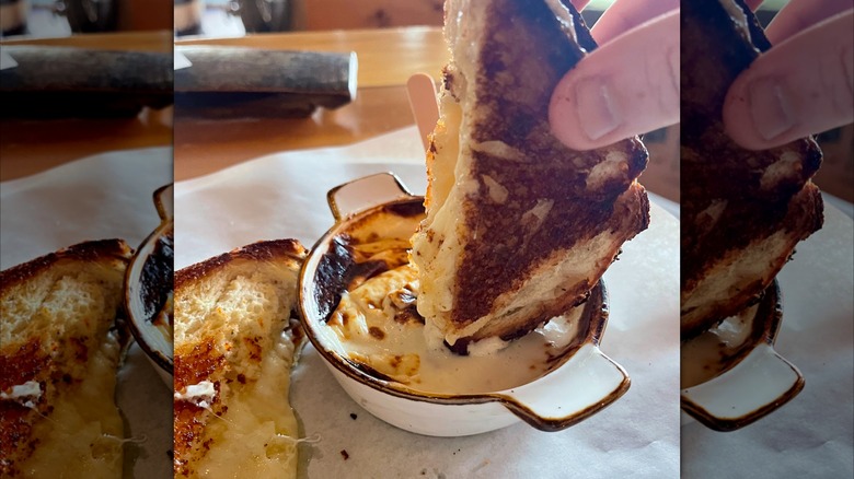 Hand dipping grilled cheese sandwich in beer cheese inside restaurant.
