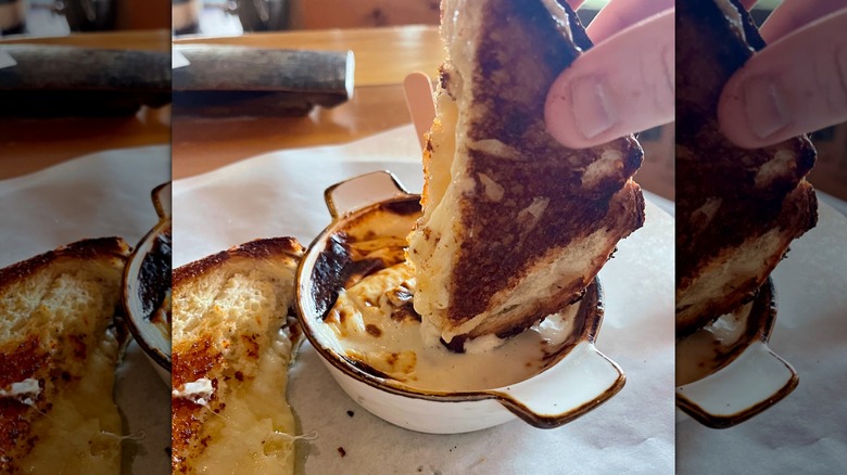 Hand dipping grilled cheese sandwich in beer cheese inside restaurant.