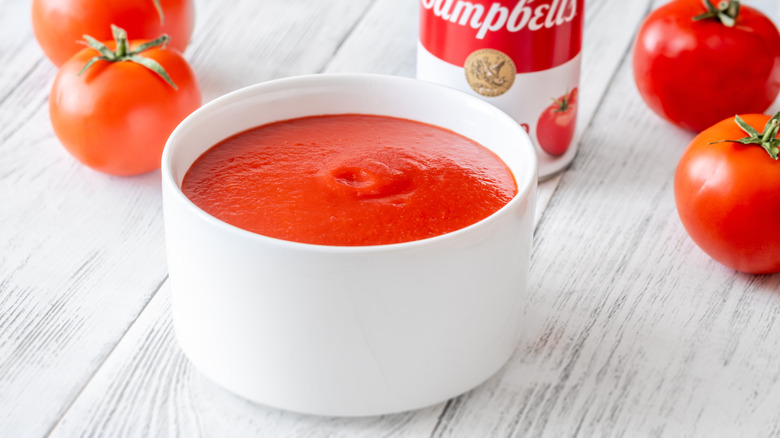 Bowl of tomato soup next to Campbell's can and whole tomatoes.