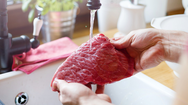 woman washes steak in a sink