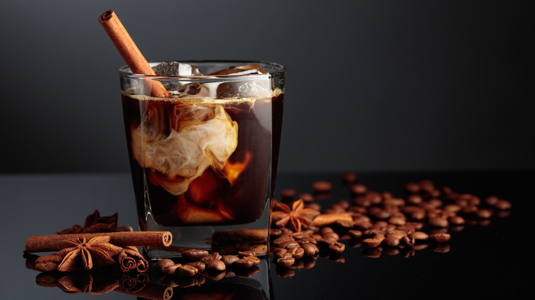 Dark liquor coffee cocktail on dark background with spices and ice plus beans nearby
