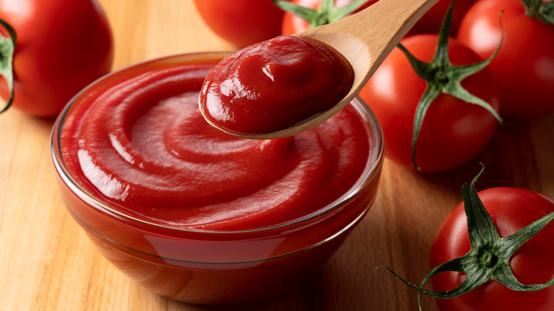 Glass bowl of ketchup surrounded by tomatoes