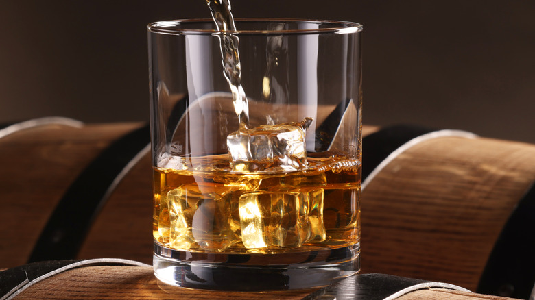 Bourbon pouring into whiskey glass on top of barrel.