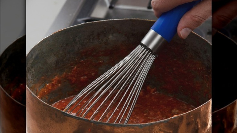 Hand stirring meat sauce in a pot with a whisk