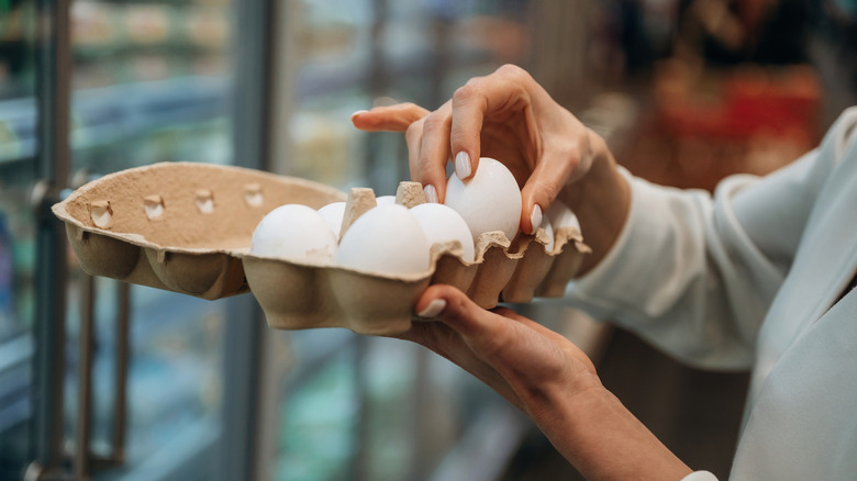Person checking eggs in a carton while shopping at a grocery store.