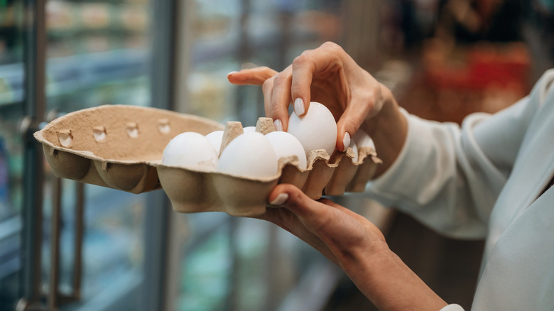 Person checking eggs in a carton while shopping at a grocery store.