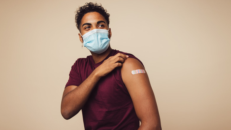 Man wearing mask shows vaccination bandaid