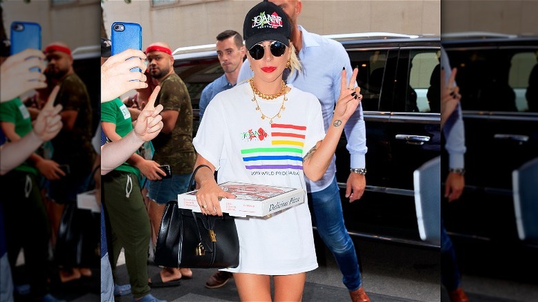 Lady Gaga in a pride T-shirt, holding a small pizza box and making a peace sign