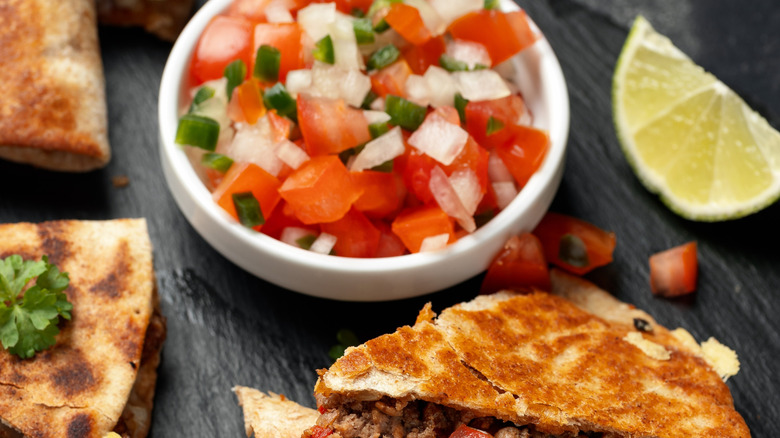 Bowl of pico de gallo next to slice of lime and quesadilla