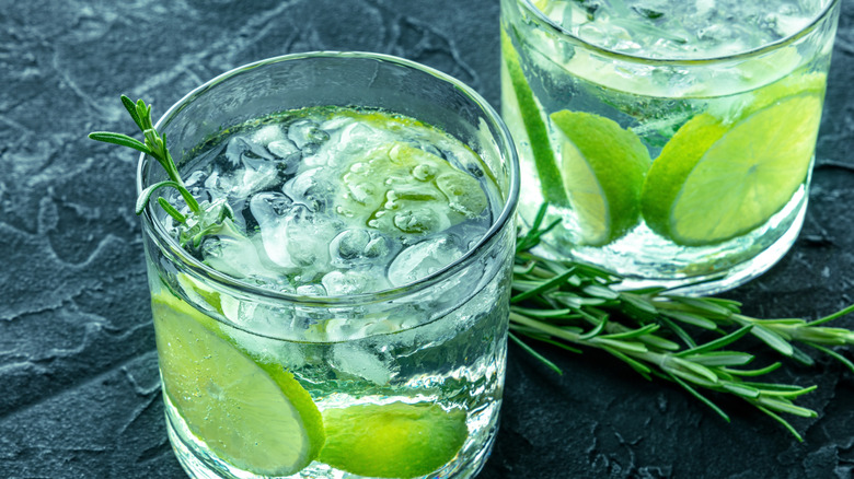 Glasses of gin and tonic with lime and rosemary on stone surface