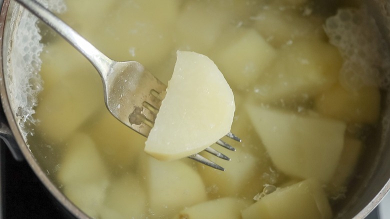Fork holding potato chunk above pot