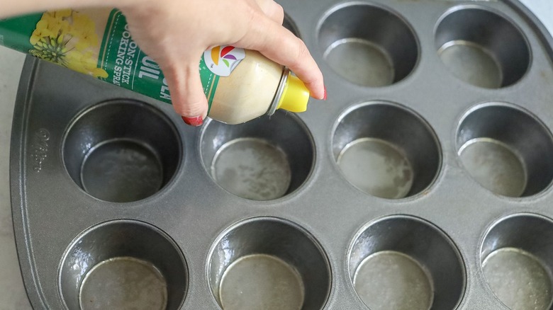 Hand spraying muffin tin with cooking spray
