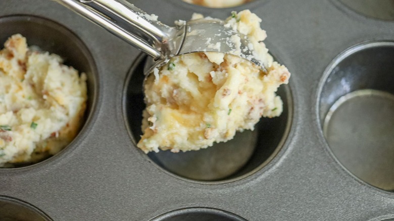 Scoop of loaded mashed potatoes going into muffin tin well