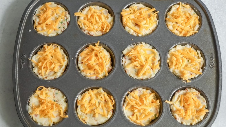 Mashed potato cups topped with shredded cheddar in muffin tin