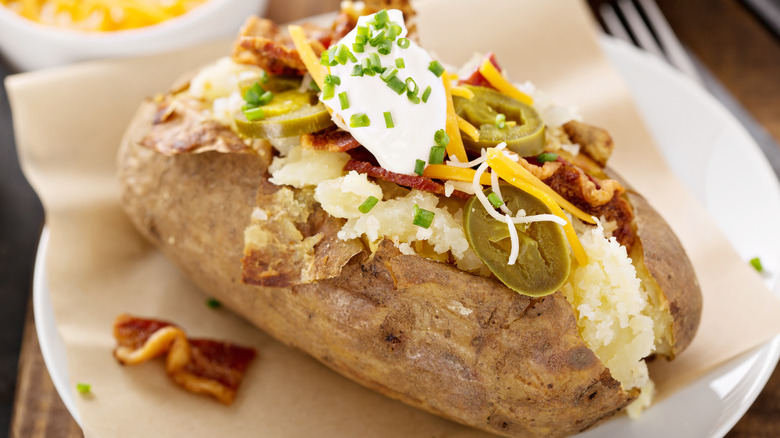 A loaded baked potato with sour cream, jalapenos, chives, and bacon