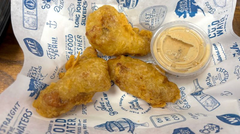Three Crispy Battered Wings on a Long John Silver's branded paper with sauce