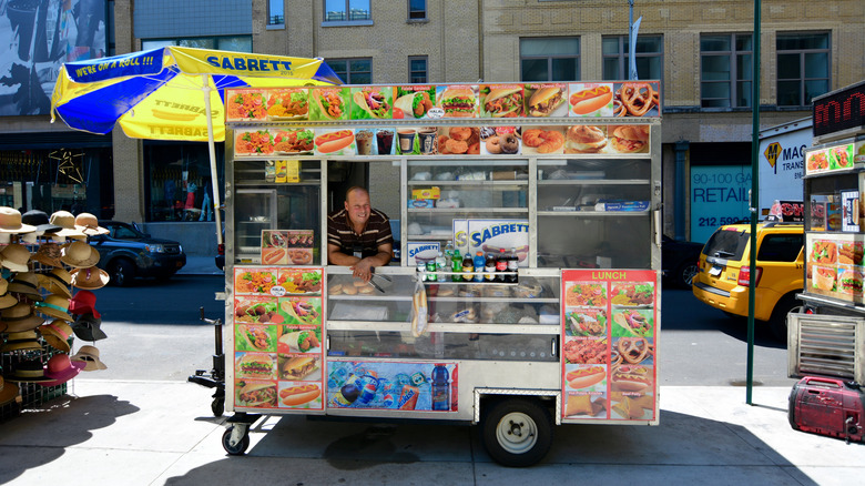 A Sabrett hot dog cart with smiling vendor on sunny day
