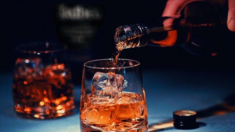Bourbon being poured into a glass with ice.