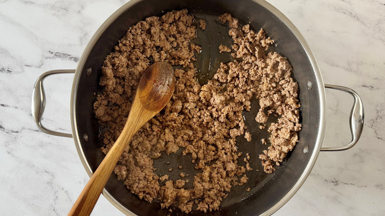 Crumbled beef and sausage mixture in skillet with wooden spoon