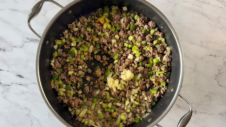 Ground meat and diced vegetable mixture in skillet with minced garlic