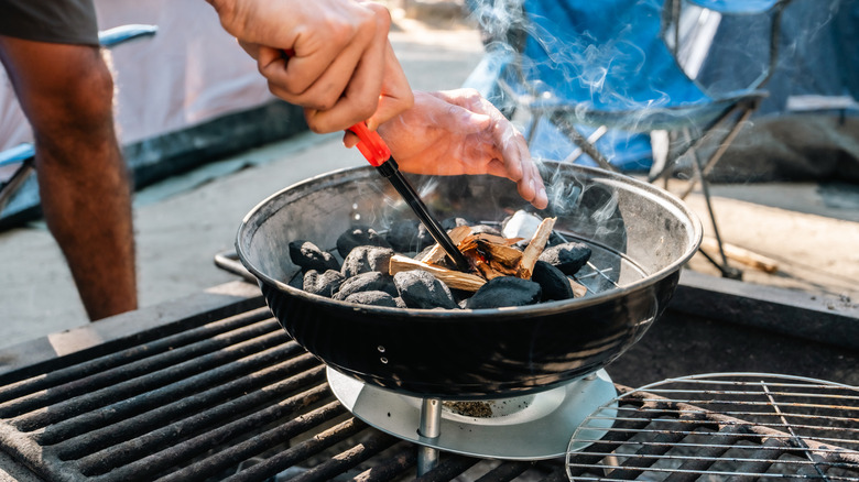 Person lighting charcoal briquettes inside metal grill
