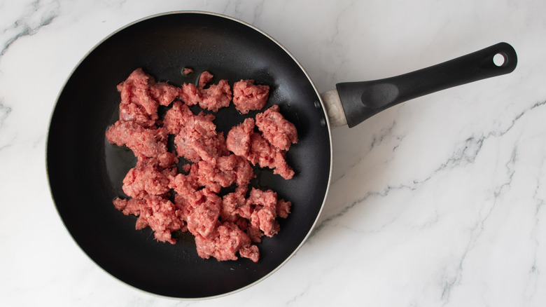 raw ground beef in a black frying pan