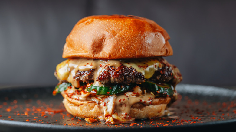 Cheeseburger with sauces and toppings surrounded by chili flakes.