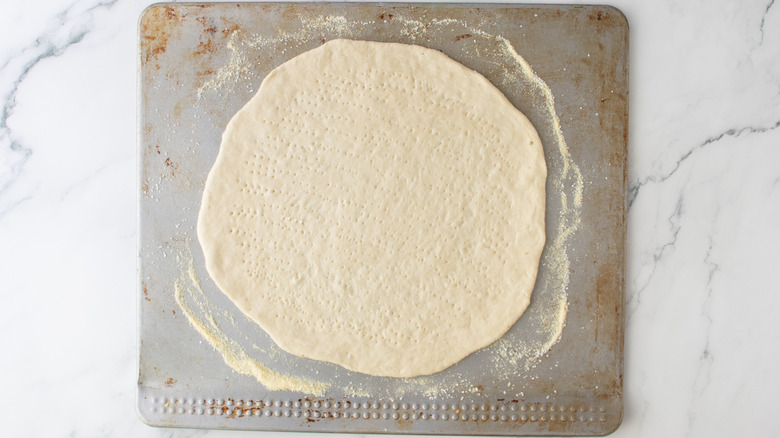 unbaked pizza crust with fork holes on a sheet pan