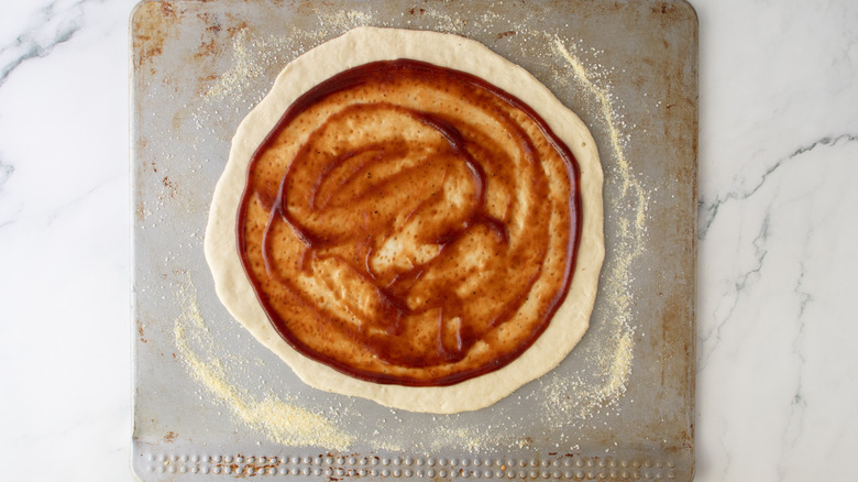 unbaked pizza crust with red sauce on a sheet pan