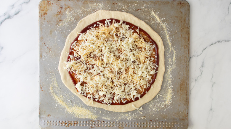 unbaked pizza crust with red sauce and cheese on a sheet pan