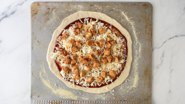 unbaked pizza crust with red sauce, chicken, and cheese on a sheet pan