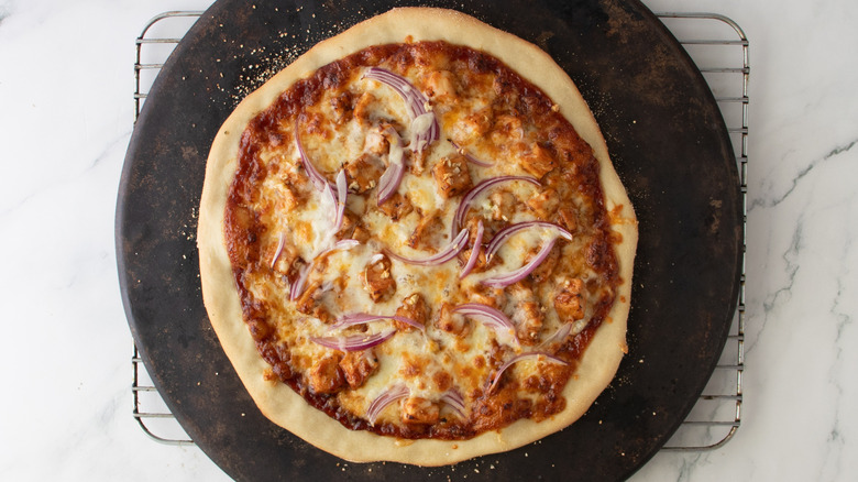 chicken and onion-topped pizza on a pizza stone