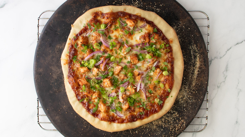chicken and green onion-topped pizza on a pizza stone