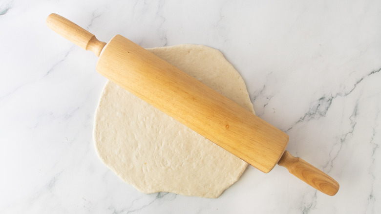 rough circle of dough underneath a rolling pin