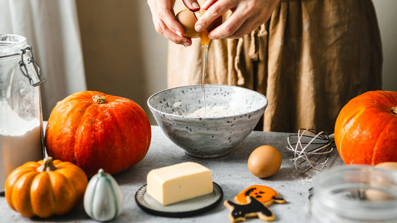 Baker surrounded by pumpkins on worktop.